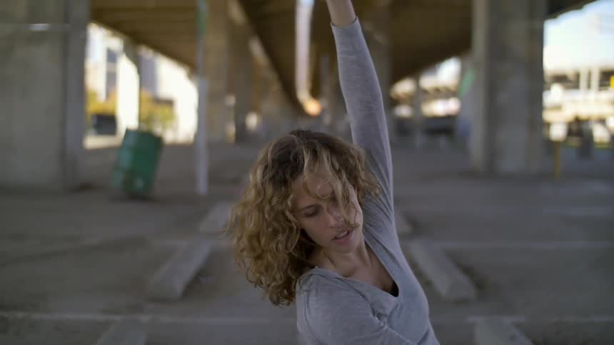A woman is doing a dance under a bridge during the day