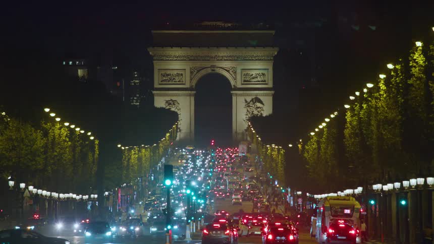 The arc de triomphe stands at the end of a bustling avenue at night