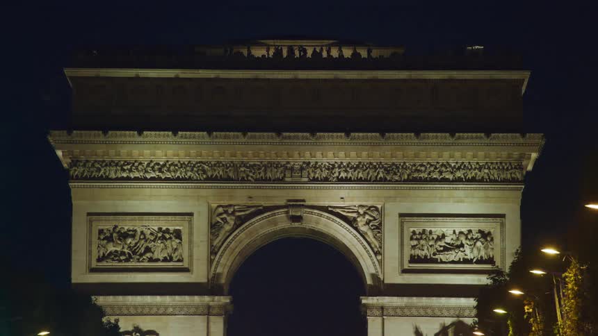 People are silhouetted on top of arc de triomphe at night
