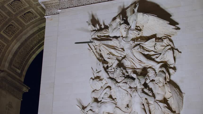 A detailed stone sculpture is attached to the arch of triumph at night