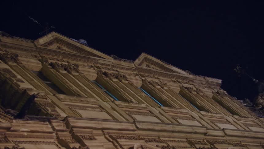 Weather vanes top large building with richly decorated facade at night