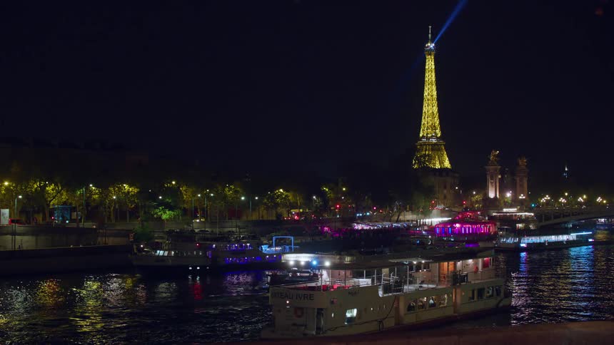 Landscape at night of a canal with tourist boats and the illuminated eiffel tower in the background