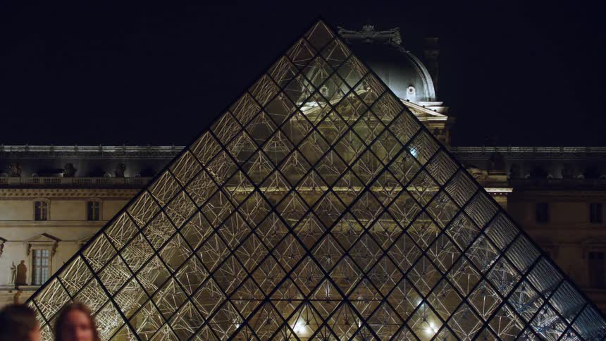 A glass pyramid outside of a building at night