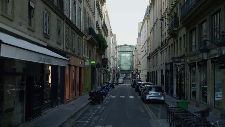 A narrow street in an european city with parked motorcycles and cars