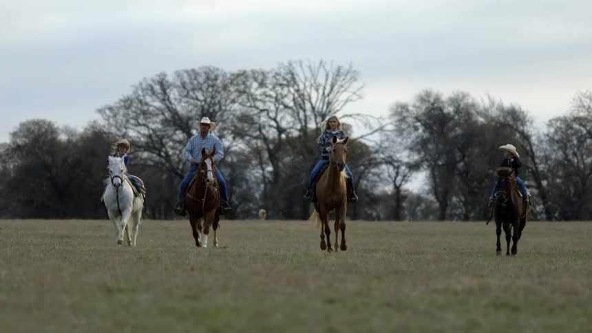 A family riding their horses at a trot across a field