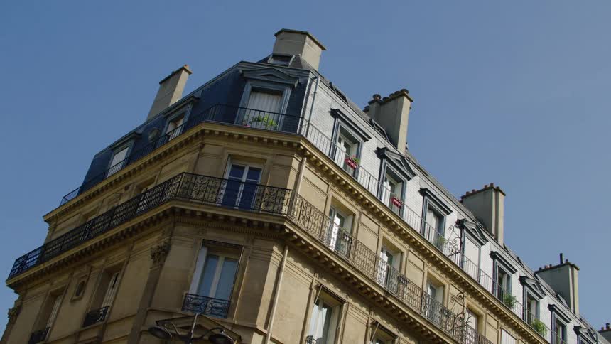 A yellow building with a gray top with many windows and balconies and the sky is very blue