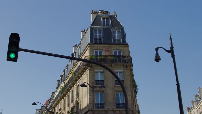A corner apartment building faces a traffic light and a bird lands on the lamppost