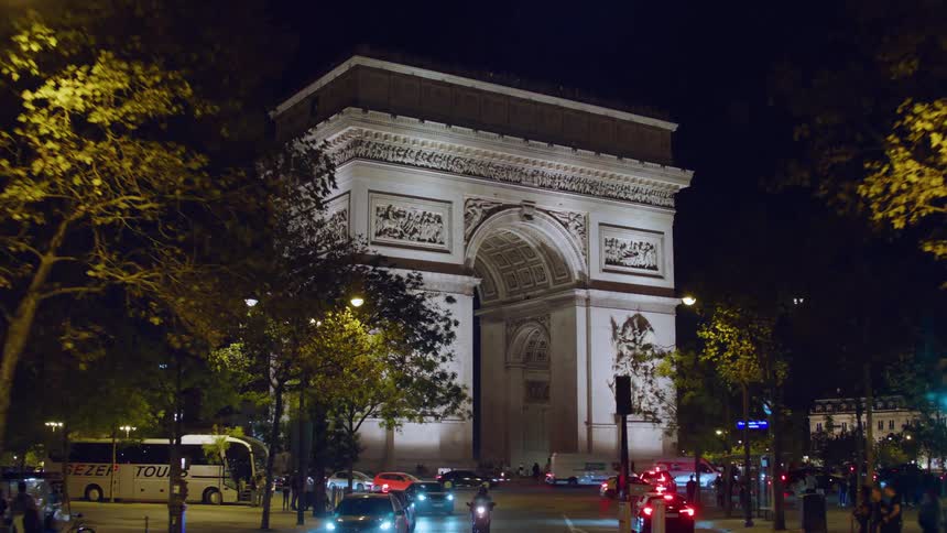 A large tourist building with a huge middle door and in a city at night with a lot of car traffic