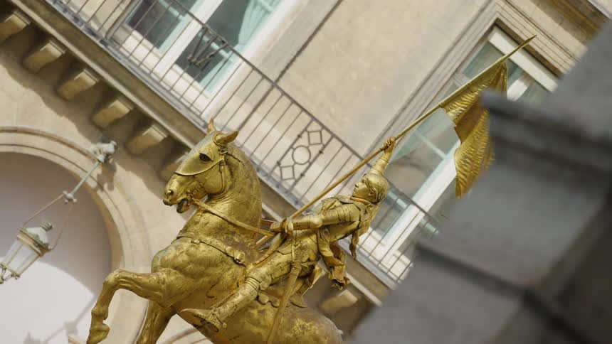 Golden statue of woman on horseback sits next to building with long walkway balcony