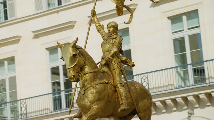 A golden statue of a knight and a horse in front of a building with windows