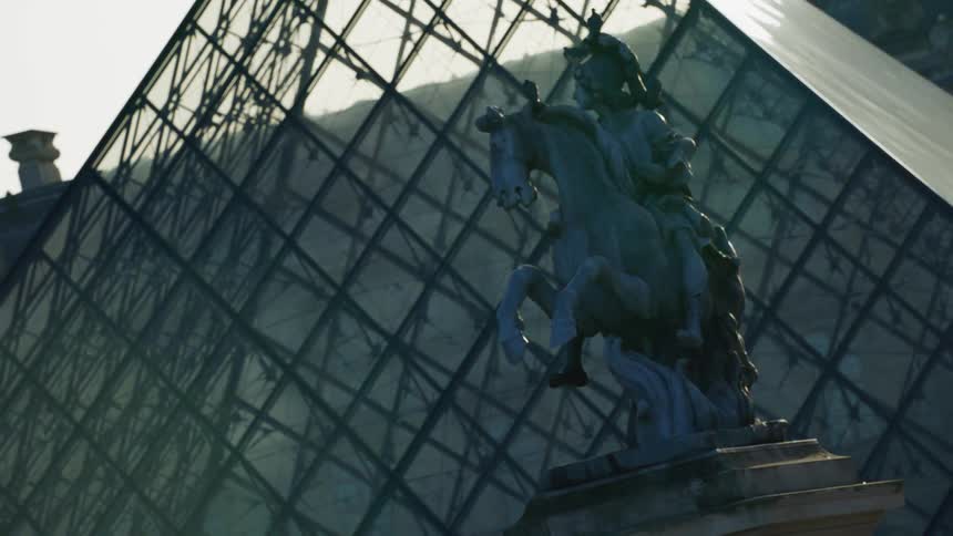 A monument of a statue of a person on top of a horse and behind a glass greenhouse