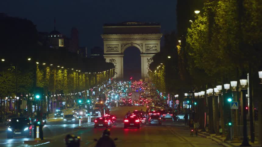 Heavy traffic on the road leading to the arc de triomphe in paris and a fair full of people in the park parallel to the road