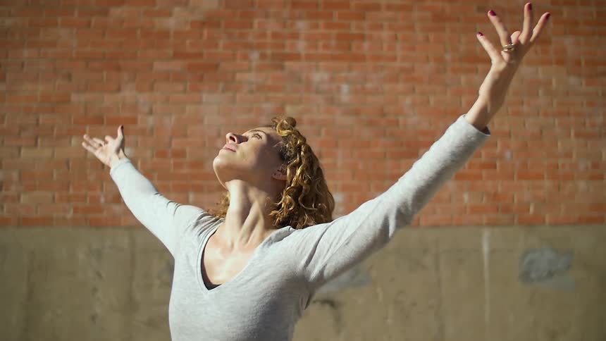 A woman is dancing in the sunlight near a brick wall