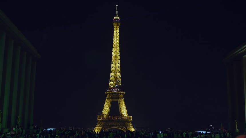 Crowd of people in front of a square overlooking the eiffel tower illuminated at night