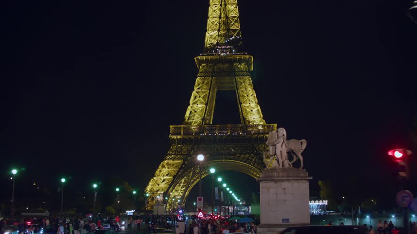 The eiffel tower is all lit up at night and in front there is a square