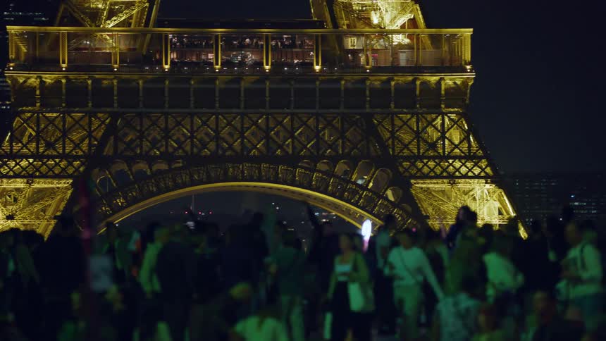 Crowd of people in a square at night facing the illuminated eiffel tower