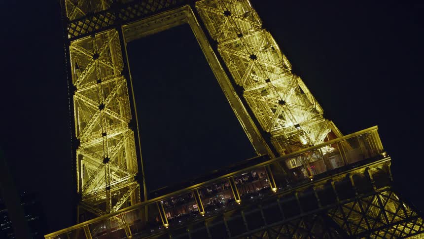 Exterior architecture of the eiffel tower illuminated at night as the crowd of people around