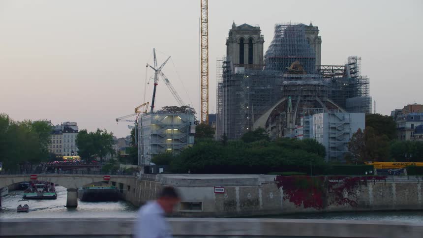 A construction with several irons and a crane and in front of a canal with a river and many people in the street