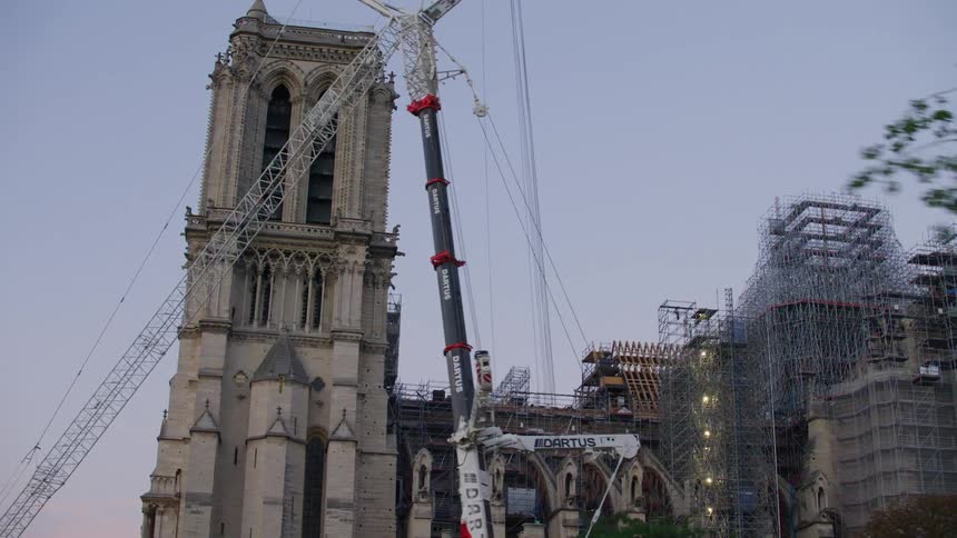 The notre dame cathedral is under restoration with scaffolding and cranes surrounding it