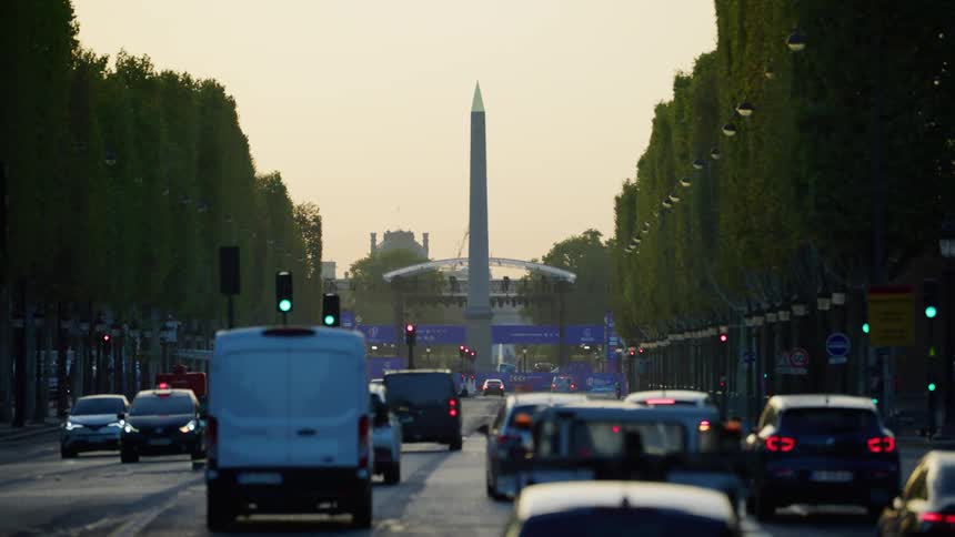 A city street with trees and an obelisk monument at sunset
