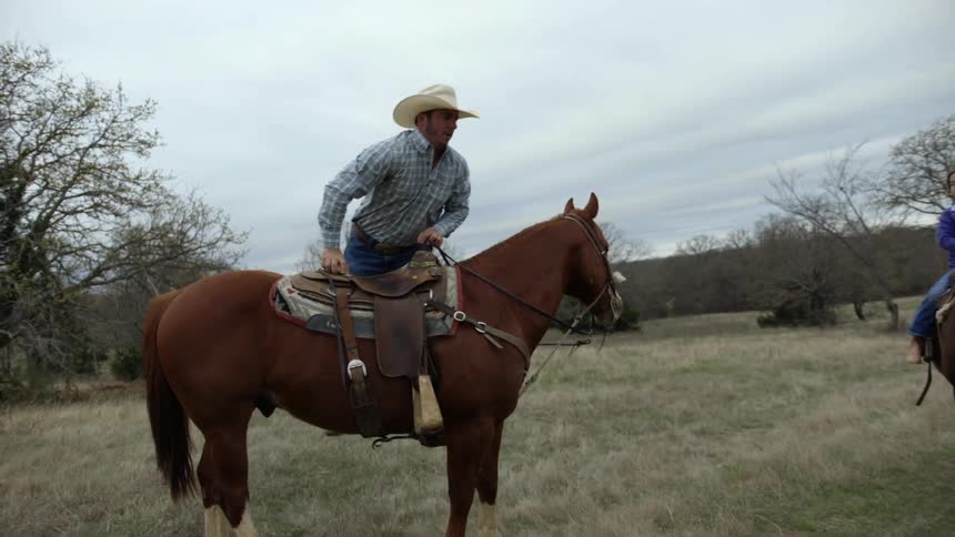 A man is getting on a horse as a child on a horse waits for him