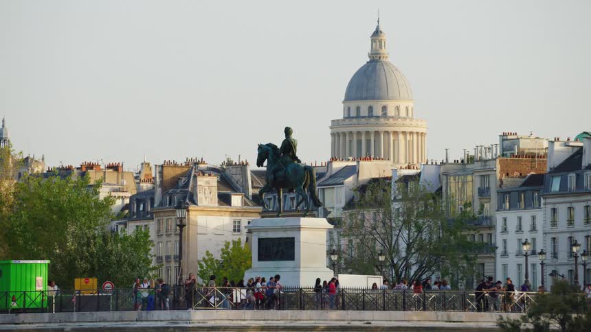 A monument of a person riding a horse and below there are several people walking on the site and right behind there is a domeshaped monastery