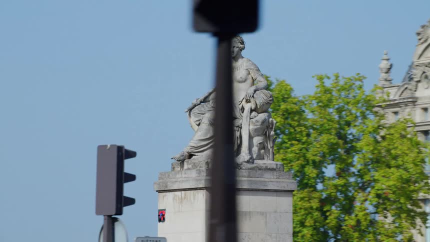 A monument of a statue of a person with a crown and is sitting and behind him there is a very wide building of ancient architecture