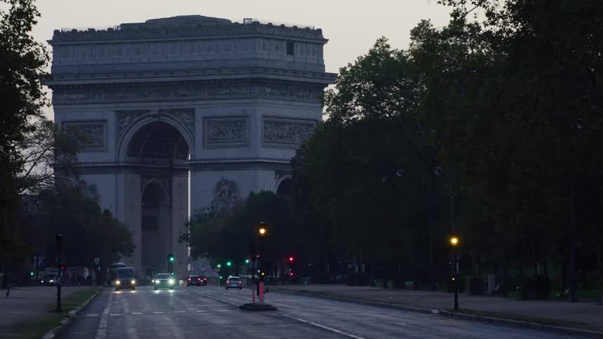 The arc de triomphe in a city where there is a street with cars passing by and people crossing the street