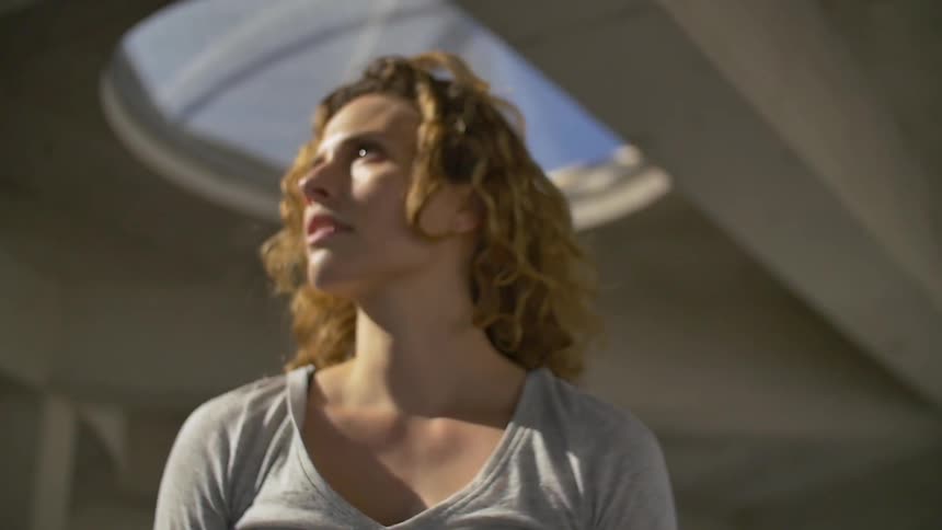 A blonde woman in a gray shirt is standing in a concrete room