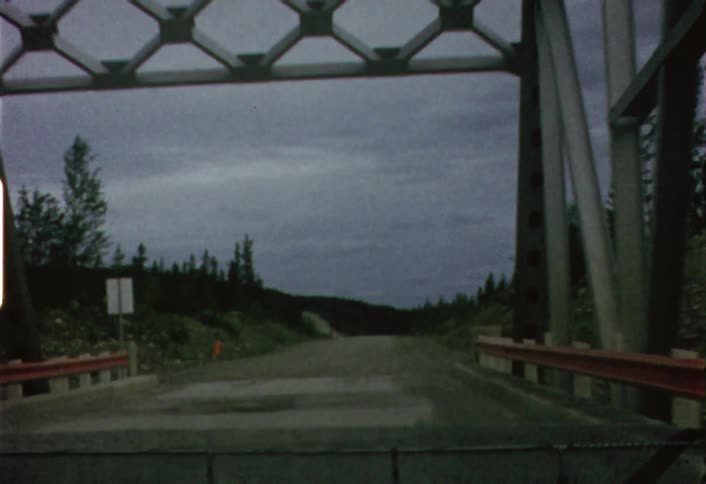 A vehicle is driving across a small bridge on a cloudy day