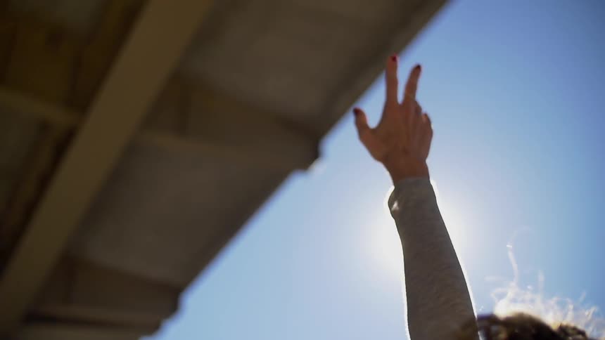 A woman is reaching her hand to the sky and the sun shines on her
