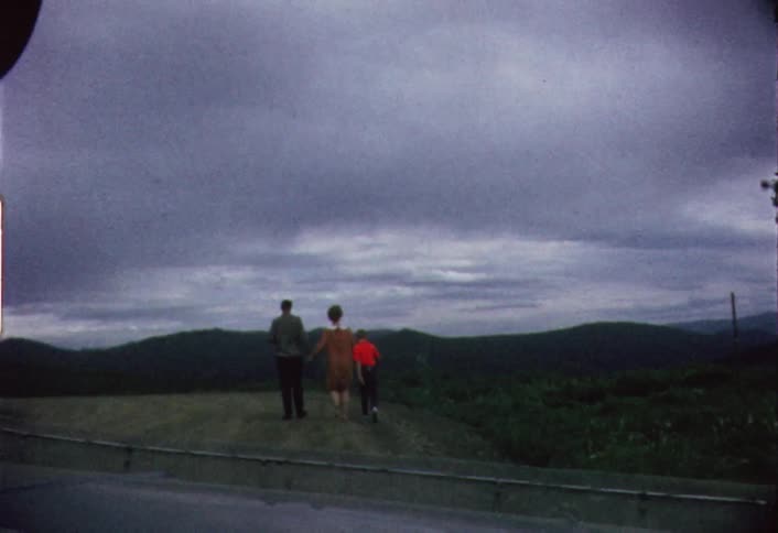Three people walking in a green pasture on a very cloudy day