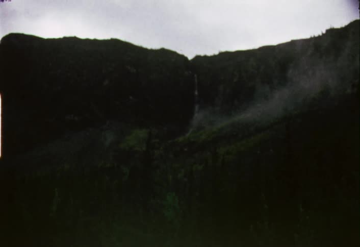 Zooming in view of a thin waterfall high from a mountain on a cloudy day