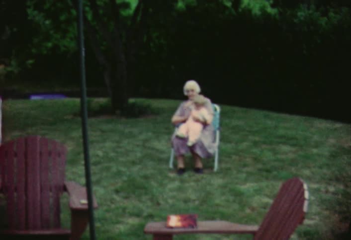 Elderly woman holding an infant while sitting in a lawn chair outdoors