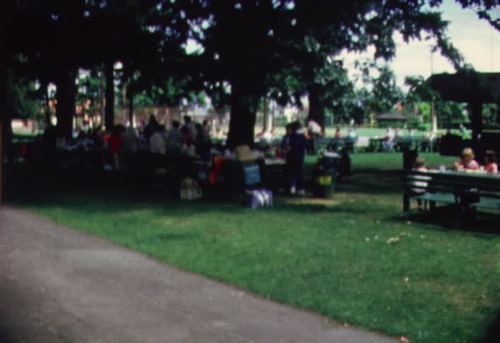 A large group of people are gathered on a grass area like a park and having a picnic