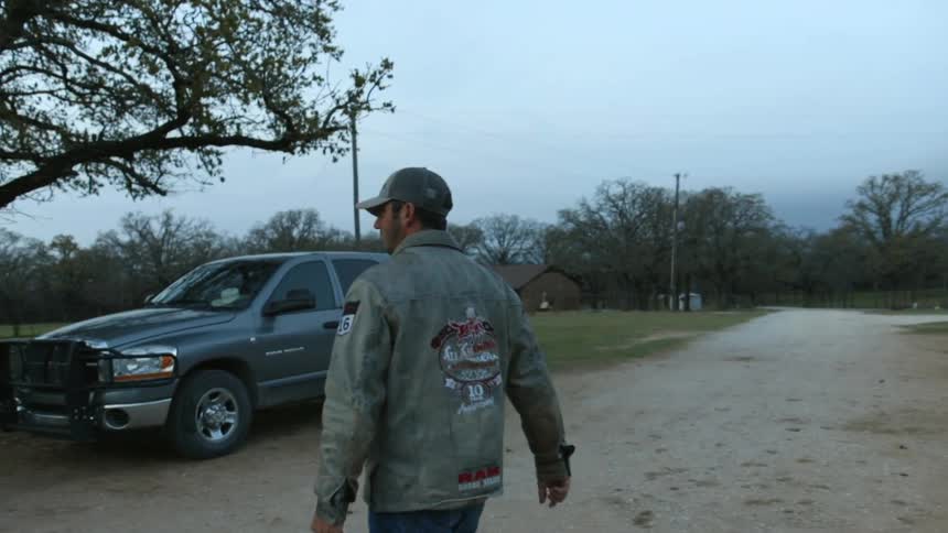 A man is carrying a bucket across a dirt driveway on a farm