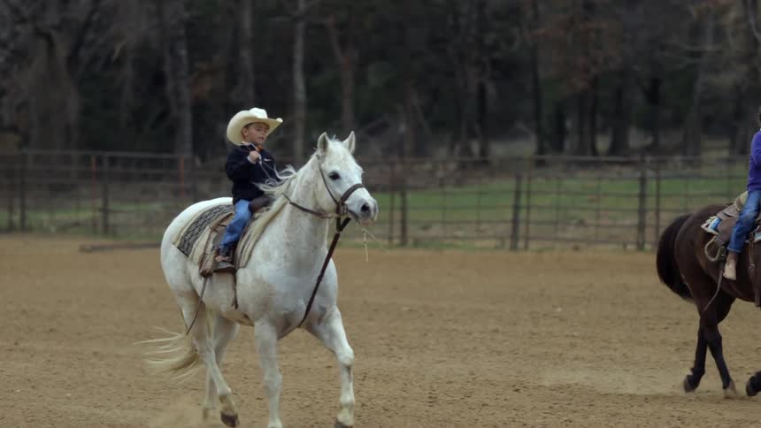Small boy and girl riding horses in a fenced area on farm