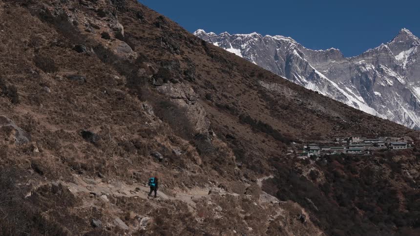 Backpacker hikes along narrow mountain trail leading to town on mountainside