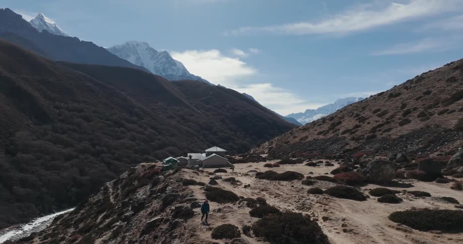 An aerial view of a man hiking in rugged terrain near a river and mountains