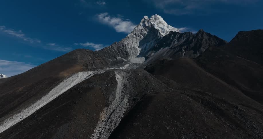 A large mountain with a snowcovered peak and in front are gravel paths that lead to the top