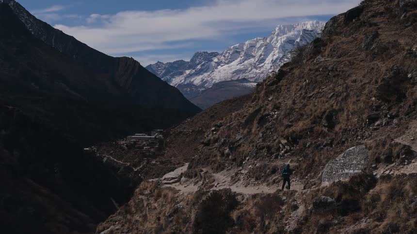 A person walking on a path that is going up a mountain and back to a huge mountain with snow on its surface