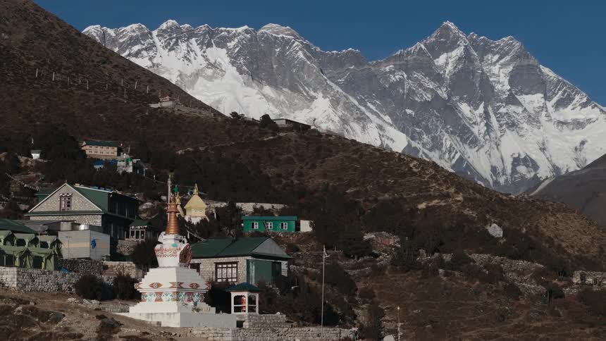Mountainside town with copper topped sculpture sits on slope with snow covered mountain in the background