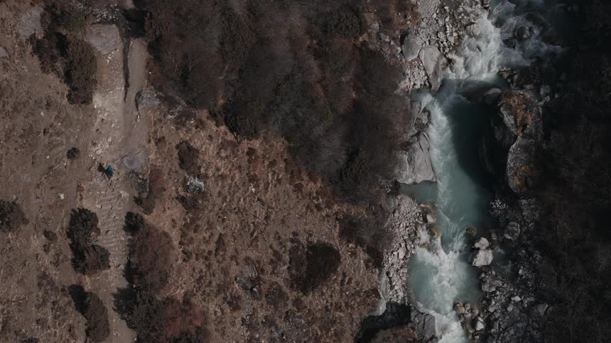 A person walks down a small path next to a river on a mountain