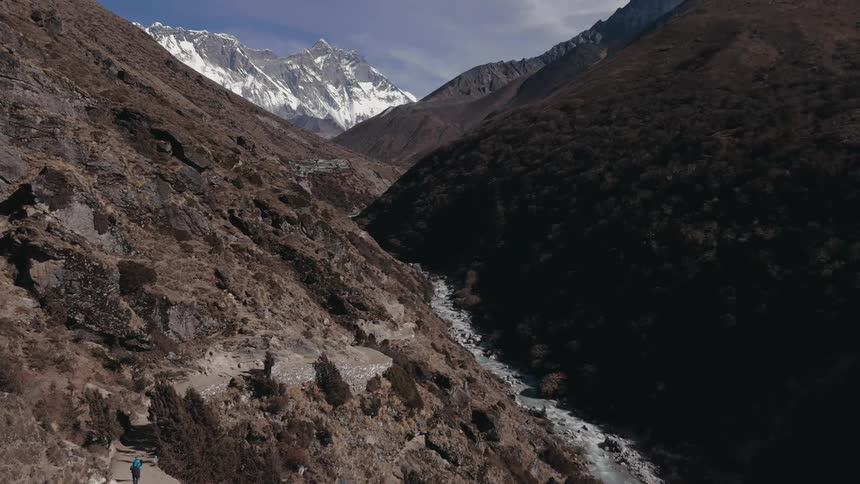 Landscape of rocky and some snowy mountain ranges with flowing river in the middle of blue with clouds