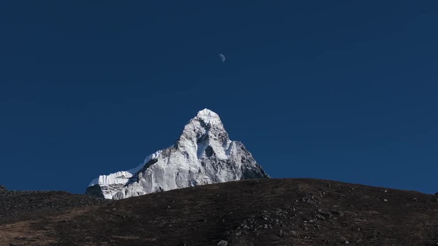 Landscape of hills and mountains with cliff and snow on a blue sky day with the moon in sight