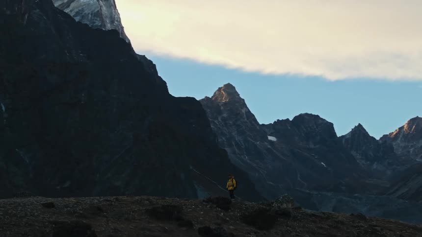 A person in a yellow jacket walking on a path and back to a huge mountain