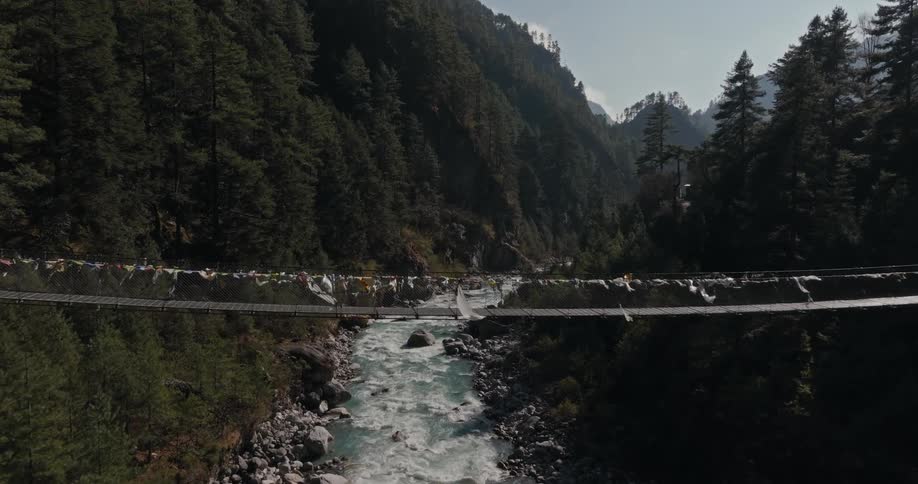 A suspension bridge with tall towers over a fastmoving river in the mountains