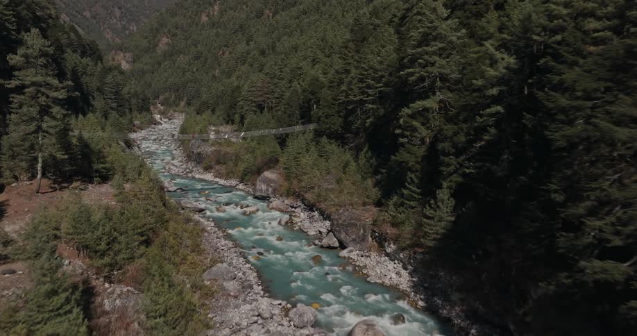 Two hikers cross a suspension bridge over a river in a mountain valley