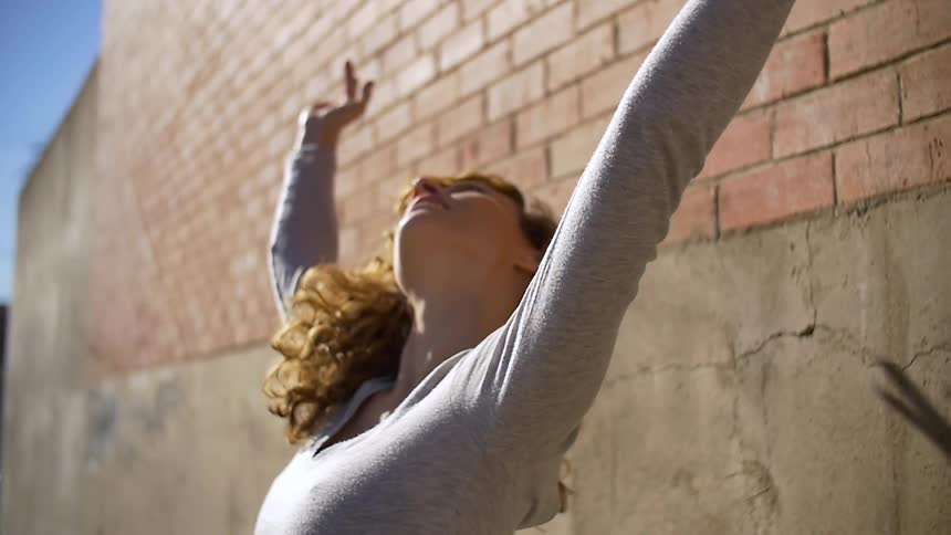 A woman is dancing by a building on a sunny day