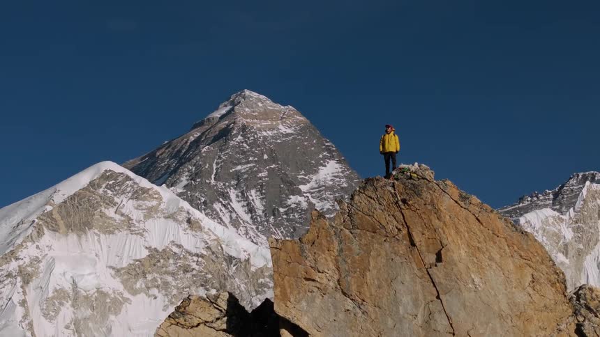 Backpacker standing on ridge near snowy mountains throws his arms into the air